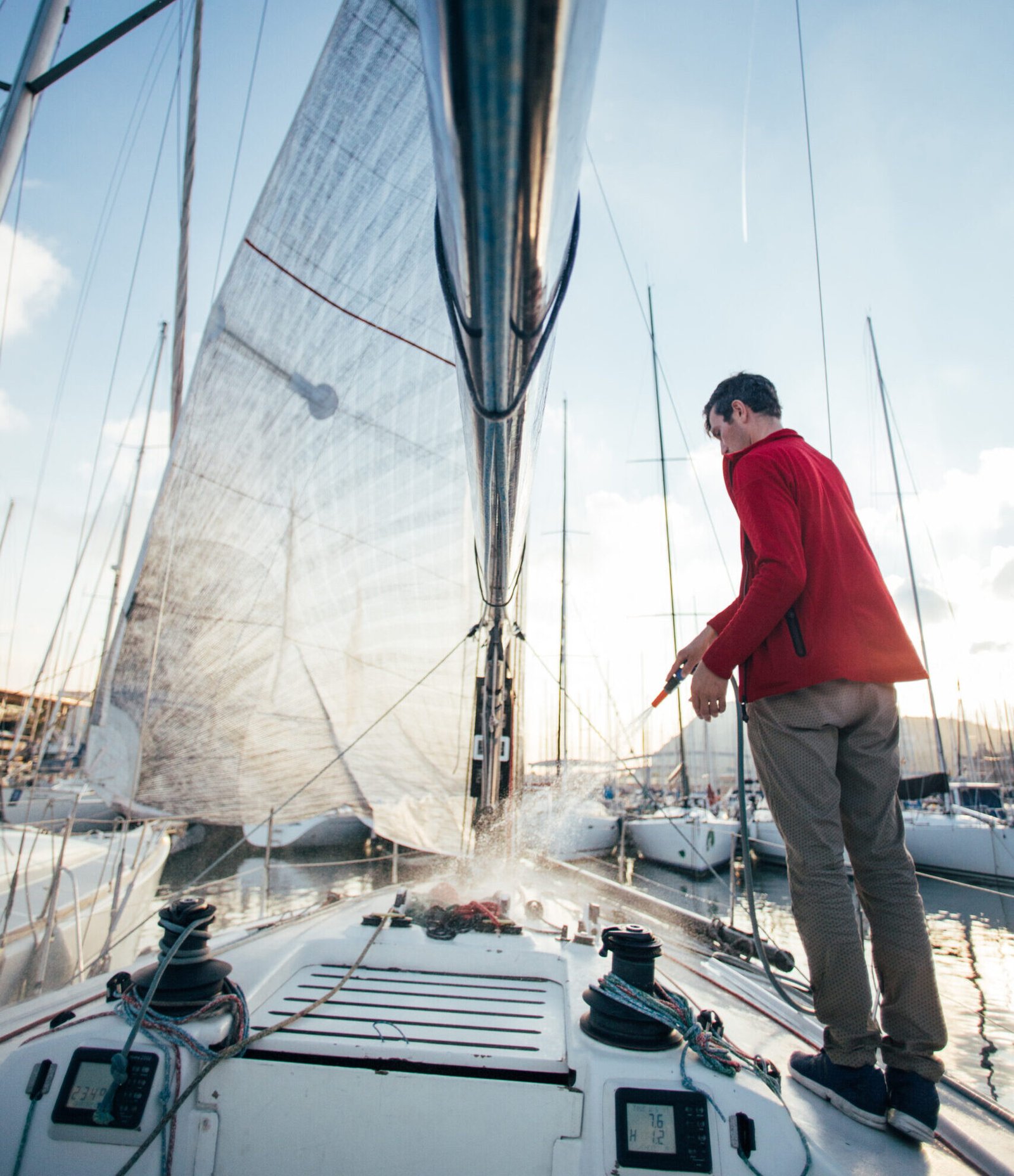 Sailboat owner or yachtsman uses hose to wash of salt water from yachr deck when docked or parked in marina on sunset, after long day of sailing race or competition